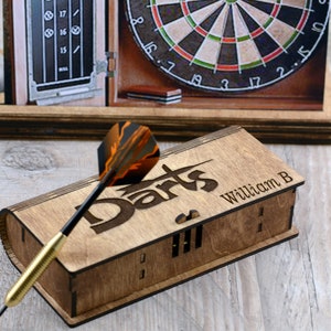May include: A wooden box with the word "Darts" engraved on the top. The box has a slot for storing darts and is personalized with the name "William B".