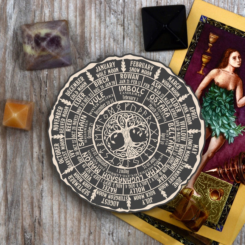 May include: A circular wooden wheel with a tree of life design in the centre. The wheel is divided into 12 sections, each representing a month of the year and a corresponding moon phase, tree, and holiday. The text on the wheel includes the names of the months, the moon phases, the trees, and the holidays. The wheel is a visual representation of the Wheel of the Year, a pagan calendar that celebrates the cycles of nature.