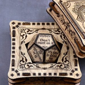 May include: A wooden box with a decorative design and a wooden dice inside. The dice has six sides with different phrases on each side, including "Don't count on it", "It is decidedly so", and "It's time to drink tea".