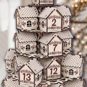 May include: A wooden advent calendar shaped like a tiered village. Each house is numbered and decorated with festive details like candy canes and snowflakes. The houses are light-colored with dark brown accents.