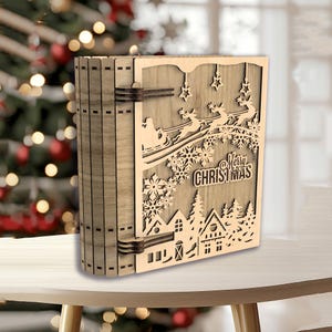 Peut inclure: Une bo&icirc;te en bois sur le th&egrave;me de No&euml;l avec un motif d&eacute;coup&eacute; au laser. Le motif repr&eacute;sente le P&egrave;re No&euml;l dans un tra&icirc;neau tir&eacute; par des rennes, des flocons de neige, des &eacute;toiles et l'inscription "Merry Christmas". La bo&icirc;te est marron clair et a l'apparence d'un livre.