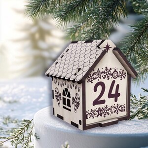 May include: A wooden Christmas advent calendar shaped like a house. The house has a brown roof and trim, with the number 24 displayed on the front. The house is decorated with snowflakes, candy canes, and a star. The background is a snowy scene with evergreen branches.