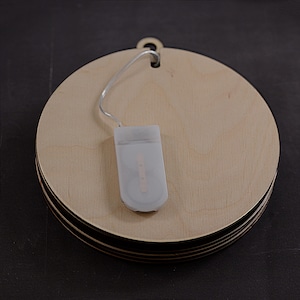 Pu&ograve; includere: Un set di tre ornamenti rotondi in legno con una stringa di luci LED bianche a batteria. Gli ornamenti sono impilati uno sopra l'altro e hanno un foro nella parte superiore per essere appesi.