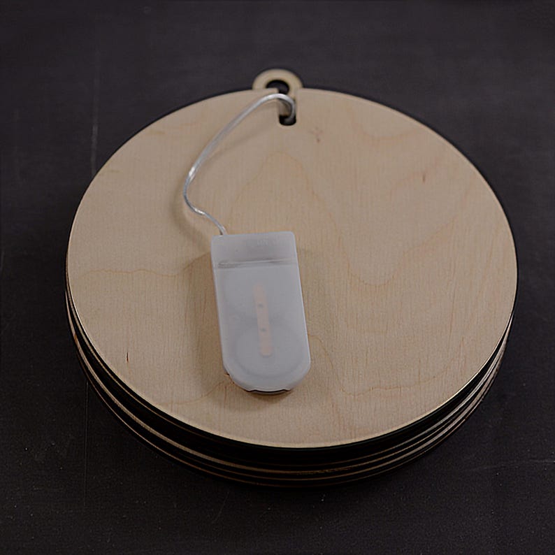 Pu&ograve; includere: Un set di tre ornamenti rotondi in legno con una stringa di luci LED bianche a batteria. Gli ornamenti sono impilati uno sopra l'altro e hanno un foro nella parte superiore per essere appesi.