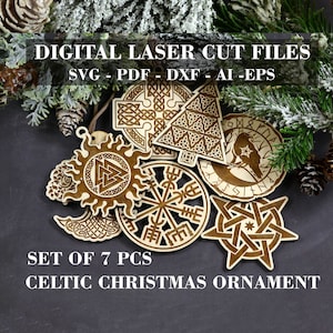 May include: Set of seven laser cut Celtic Christmas ornaments. The ornaments are made of wood and feature various Celtic designs, including a sun, a tree, a cross, a raven, a compass, a star, and a crescent moon. The ornaments are arranged on a dark grey surface.