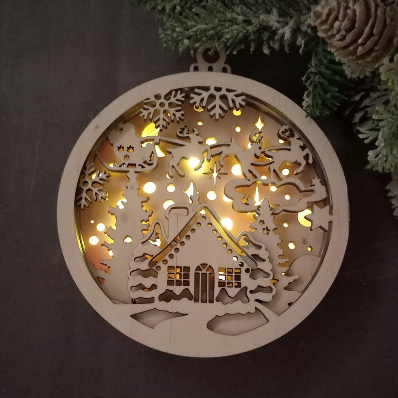 Pu&ograve; includere: Un ornamento natalizio in legno con un design illuminato. L'ornamento presenta una casa, alberi e una slitta di Babbo Natale con renne. L'ornamento &egrave; illuminato da luci LED bianco caldo.