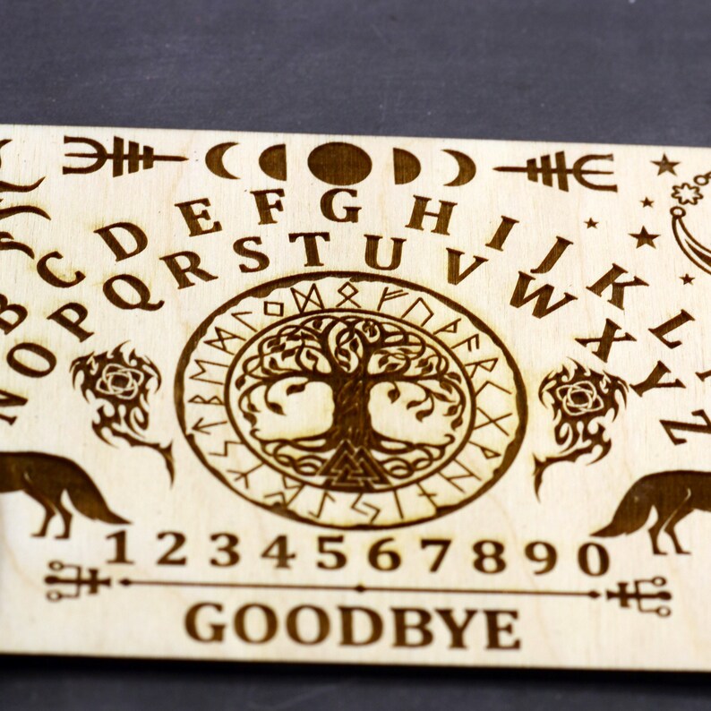 K&ouml;nnte beinhalten: Ein Ouija-Brett aus Holz mit einem Lebensbaum-Design in der Mitte. Das Brett enth&auml;lt das Alphabet, die Zahlen 1-9 und 0 sowie die W&ouml;rter "GOODBYE" und "YES".