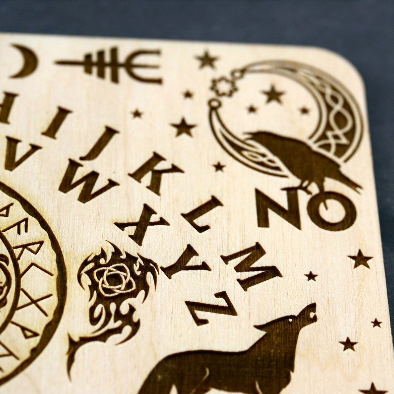 K&ouml;nnte beinhalten: Ein Ouija-Brett aus Holz mit einem Halbmond, Sternen, einem Raben und einem Wolf. Das Brett enth&auml;lt die Buchstaben des Alphabets, die Zahlen 0-9 und die W&ouml;rter "ja", "nein" und "auf Wiedersehen".