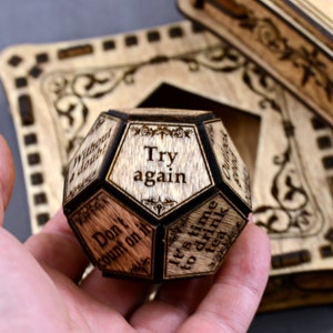 May include: Wooden cube with eight sides, each with a different inspirational message. The cube is engraved with the phrases "Try again", "Don't count on it", "It's time to drink tea", "Without a doubt", "Outlook good", and more.
