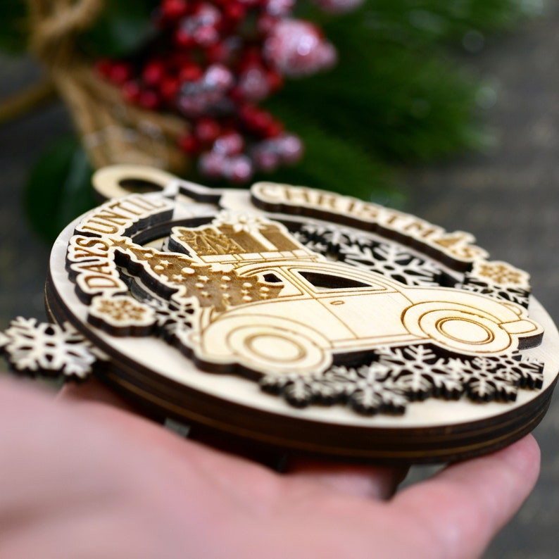 Puede incluir: Adorno de madera para la cuenta atr&aacute;s de Navidad con un coche vintage que lleva un &aacute;rbol de Navidad y regalos. El adorno est&aacute; decorado con copos de nieve y el texto "Days Until Christmas".