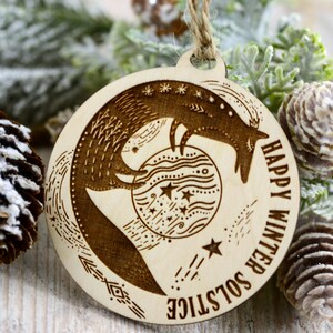 May include: A wooden ornament with a fox design holding a moon with stars. The ornament is inscribed with the text "Happy Winter Solstice".