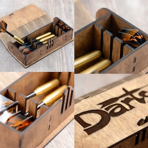 May include: A wooden box with a hinged lid for storing darts. The box has a compartment for the darts and a separate compartment for the dart flights. The box is engraved with the word "Darts".