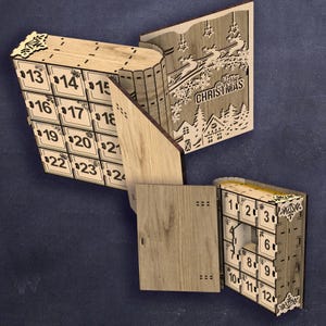 Peut inclure: Un calendrier de l'Avent en bois en forme de livres ouverts. Le calendrier comporte 24 compartiments num&eacute;rot&eacute;s, avec des motifs d&eacute;coup&eacute;s au laser d'une sc&egrave;ne de No&euml;l et des accents d&eacute;coratifs. Les chiffres sont en noir.