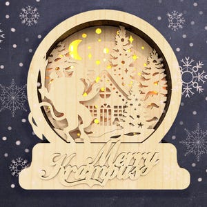 May include: A wooden Christmas snow globe with a light-up scene of Krampus standing in a snowy forest with a house and a crescent moon. The base of the snow globe reads "Merry Krampus".