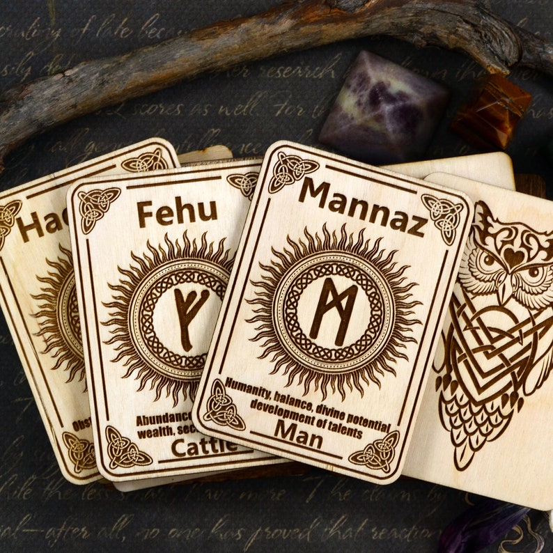 May include: Four wooden rune cards with a sun and a rune symbol on each card. The cards are labeled "Hagal", "Fehu", "Mannaz", and "Cattie".