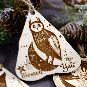 May include: Wooden Christmas ornament with a laser-etched design of an owl, moon, and stars. The ornament is painted brown and has the words "Blessed" and "Yule" inscribed on it.