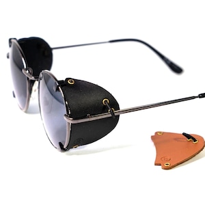 Peut inclure: Lunettes de soleil de style aviateur en cuir noir avec une monture en métal et des protections latérales. Trois protections latérales supplémentaires sont présentées en cuir marron, vert et noir.