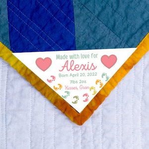 May include: A white triangle-shaped tag with pink hearts, colorful footprints, and the text "Made with love for Alexis Born April 20, 2022 7lbs 2oz Kisses, Gran".