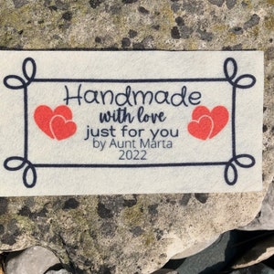 May include: Handmade with love just for you by Aunt Marta 2022. A white felt tag with a black border and two red hearts.