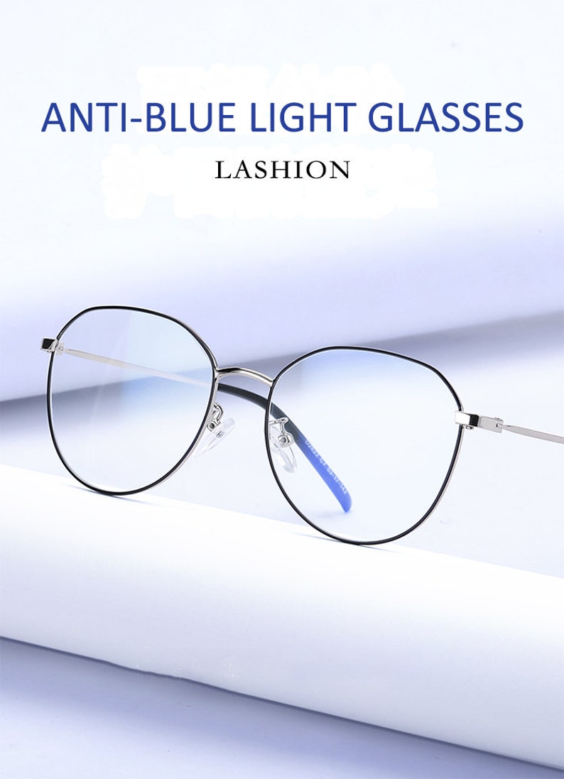 Puede incluir: Gafas redondas de bloqueo de luz azul con montura plateada y puente nasal azul. Las gafas est&aacute;n sobre una superficie blanca. ANTI-BLUE LIGHT GLASSES LASHION