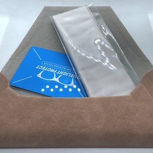 Puede incluir: Una funda de ante marr&oacute;n que contiene una tarjeta azul que dice "Bluelight Protect Blue Ray Blocker Tester" y un pa&ntilde;o de microfibra blanco.