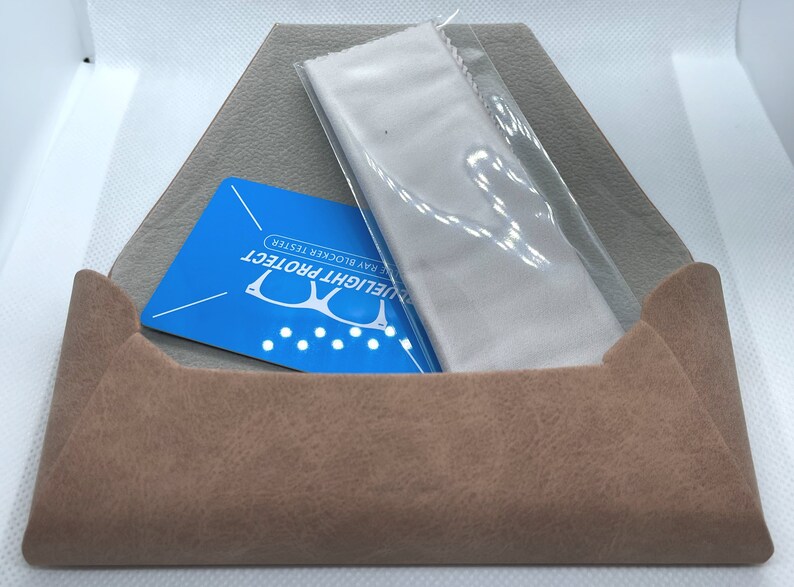 Puede incluir: Una funda de ante marr&oacute;n que contiene una tarjeta azul que dice "Bluelight Protect Blue Ray Blocker Tester" y un pa&ntilde;o de microfibra blanco.