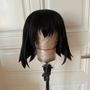 May include: A black wig with a straight, blunt cut and bangs. The wig is on a styrofoam head and a black stand.
