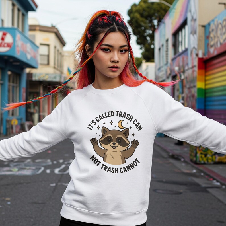 May include: White sweatshirt with a raccoon graphic and the text "IT'S CALLED TRASH CAN NOT TRASH CANNOT". The raccoon is brown and tan with its arms raised. The sweatshirt is a crew neck style.