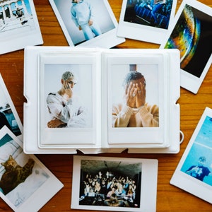 May include: A white photo album with two open pages. The left page shows a photo of a person with short brown hair wearing a white shirt. The right page shows a photo of a person with short brown hair wearing a beige sweater. The person in the photo on the right is covering their face with their hands.