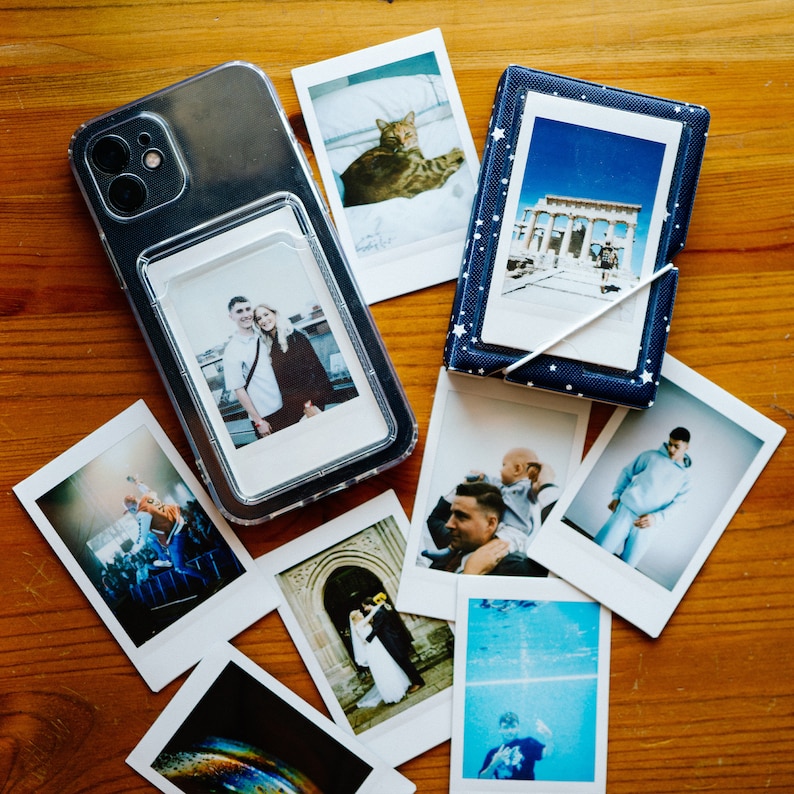 May include: A clear plastic photo album with a variety of photos inside. The photos include a couple, a cat, a building, and a person in a pool. The album is on a wooden surface.