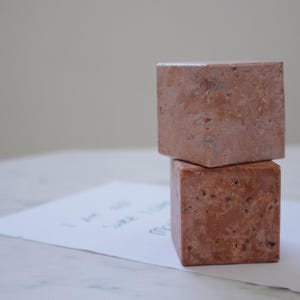 Può includere: Due blocchi quadrati impilati in travertino marrone chiaro. I blocchi sono ruvidi e hanno un aspetto naturale e rustico.