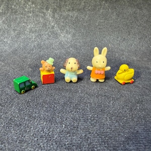 May include: A collection of miniature toy figures, including a green car, a bear on a block, a dog, a rabbit, and a duck. The figures are brightly colored and appear to be made of plastic.