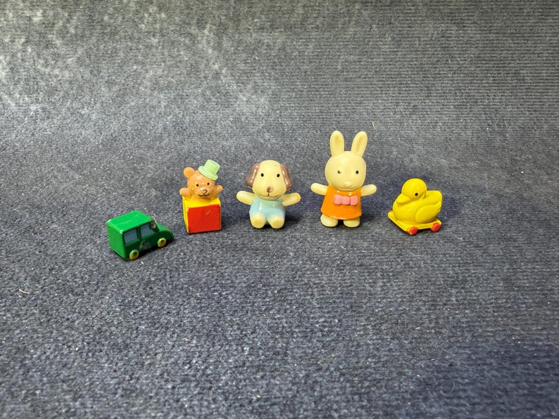 May include: A collection of miniature toy figures, including a green car, a bear on a block, a dog, a rabbit, and a duck. The figures are brightly colored and appear to be made of plastic.
