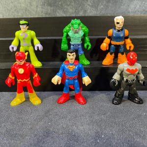 Puede incluir: Colección de figuras de acción de superhéroes coloridas, incluyendo The Flash y Superman. Las figuras están en varias poses y presentan diseños detallados, con colores vibrantes y disfraces de personajes distintivos.