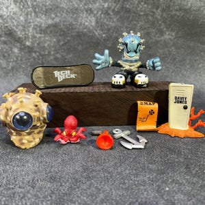 Könnte beinhalten: Eine Sammlung von Miniaturspielzeugen, darunter eine blau-schwarze Actionfigur, ein Tech Deck Skateboard und verschiedene Figuren zum Thema Nautik. Das Set enthält eine Karte, einen Anker und einen Taucherhelm.