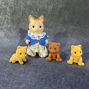 May include: A collection of miniature animal figurines. A cat figure in a blue jacket and floral dress stands with two yellow bear cubs and a brown bear cub. The figurines are made of a soft, flocked material.