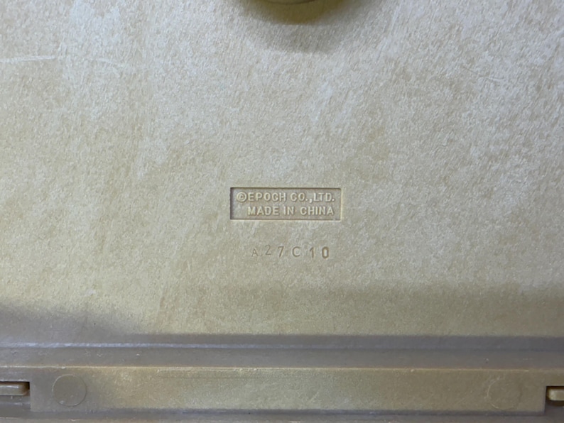 May include: Close-up of a beige plastic surface with the embossed text "EPOCH CO., LTD. MADE IN CHINA" and the numbers "A27 C10". The surface has a slightly textured appearance.