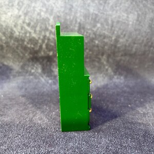 Op de afbeelding: Een groene miniatuurkast met drie lades en goudkleurige knoppen. De kleine kast heeft een rechthoekige vorm en een kleine, verhoogde bovenkant. Het stuk is geschilderd in een heldere, effen groene kleur.
