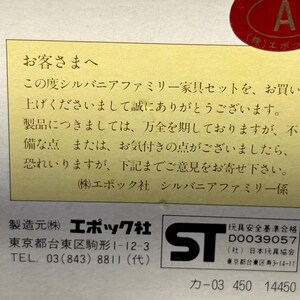 Op de afbeelding: Een close-up van een doos met Japanse tekst en een rode ronde sticker. De tekst staat op een gele achtergrond en bevat de informatie van de fabrikant en een veiligheidsmerk.