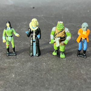 May include: Four small plastic action figures from the Star Wars franchise. The figures are of a female human in green, a human male in black and blue, a green reptilian creature, and a human male in orange and blue.
