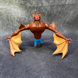 Puede incluir: Figura de acción marrón de una criatura parecida a un murciélago con alas extendidas. La figura tiene un torso musculoso, pantalones cortos azules y alas naranjas. Las alas están extendidas y los brazos son articulados.