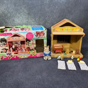May include: A Calico Critters preschool playset with a box and a building. The box is decorated with images of the playset and characters. The building has a sign that says "Preschool". Several miniature animal figures and furniture are included.
