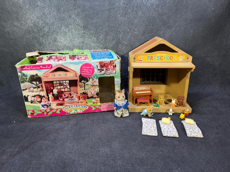 May include: A Calico Critters preschool playset with a box and a building. The box is decorated with images of the playset and characters. The building has a sign that says "Preschool". Several miniature animal figures and furniture are included.