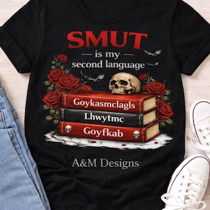 May include: Black t-shirt with the text "SMUT is my second language" in red. The graphic includes a skull atop a stack of books, surrounded by red roses and bats. The books have skull and crossbones on them.