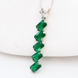 May include: A silver necklace with a pendant featuring a cascade of six emerald green gemstones.