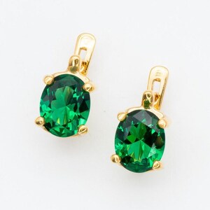 May include: A pair of gold earrings with oval-shaped green gemstones.