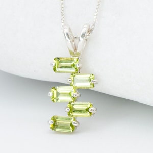 May include: A silver chain necklace with a pendant featuring five green peridot gemstones in a staggered rectangular shape.