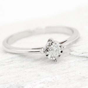 May include: A simple silver band ring with a small, round, clear diamond set in a prong setting.