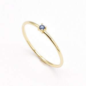 May include: A delicate gold band ring with a small, round blue sapphire gemstone.