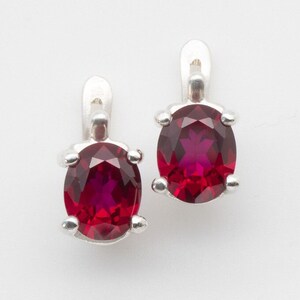May include: A pair of silver earrings with red oval-shaped gemstones.